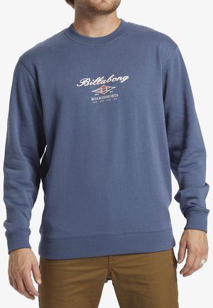 Sweatshirt bleu à manches longues avec des poignets côtelés. Présente un logo et un texte blancs sur le devant. Fabriqué en tissu doux et texturé.