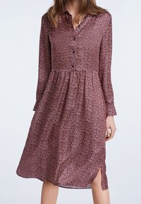 Robe à manches longues boutonnée de couleur bordeaux foncé avec un petit imprimé floral. Jupe fluide avec des fentes latérales, confectionnée dans un tissu léger.
