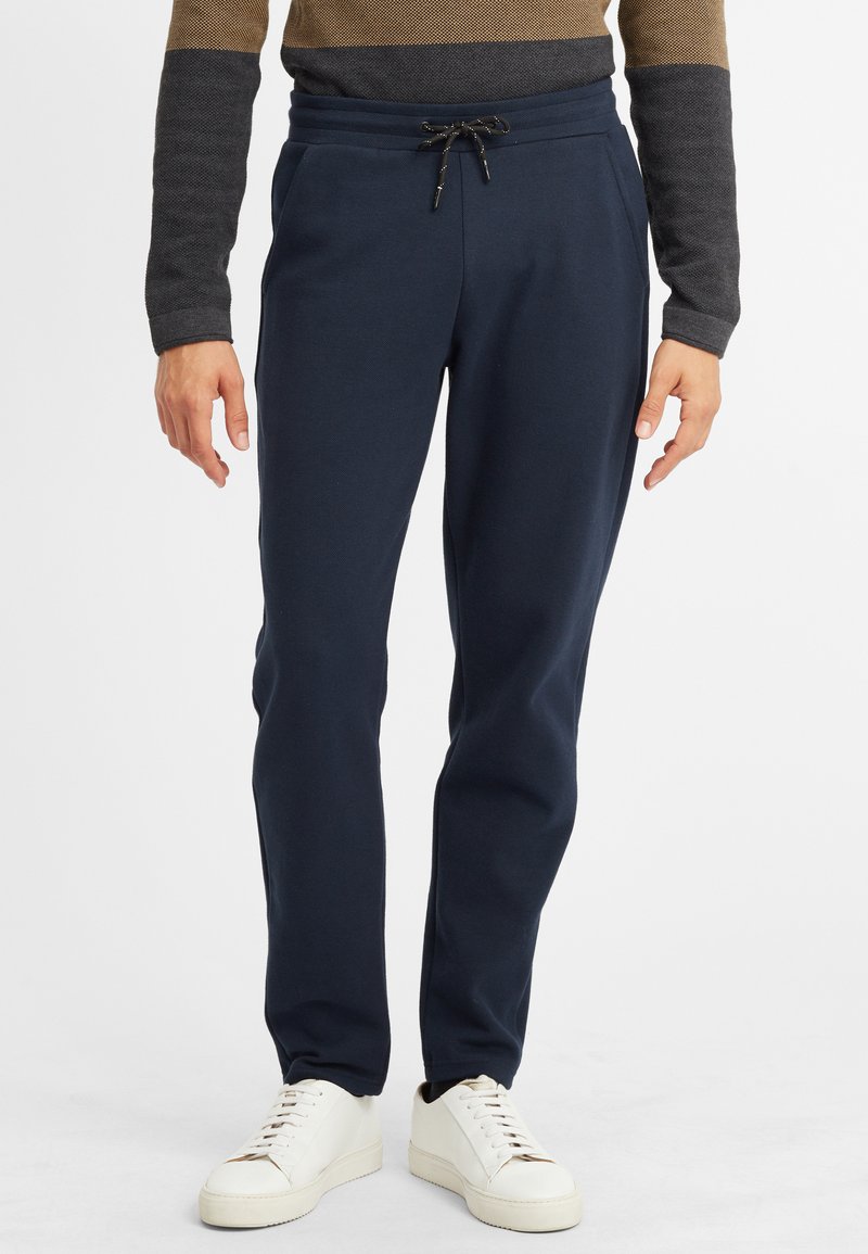 Navybyxor i mjukis med dragsko i midjan, avsmalnande ben och sidofickor. Kombinerat med vita sneakers för en avslappnad stil.