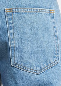 Light blue denim fabric, featuring a back pocket with a slightly textured finish and orange stitching accents along the seams.