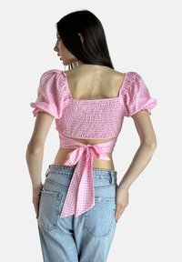 Rosa Gingham-Crop-Top mit Puffärmeln, einem gerafften Mieder und einem gebundenen Rücken. Kombiniert mit hochtaillierten blauen Jeans.