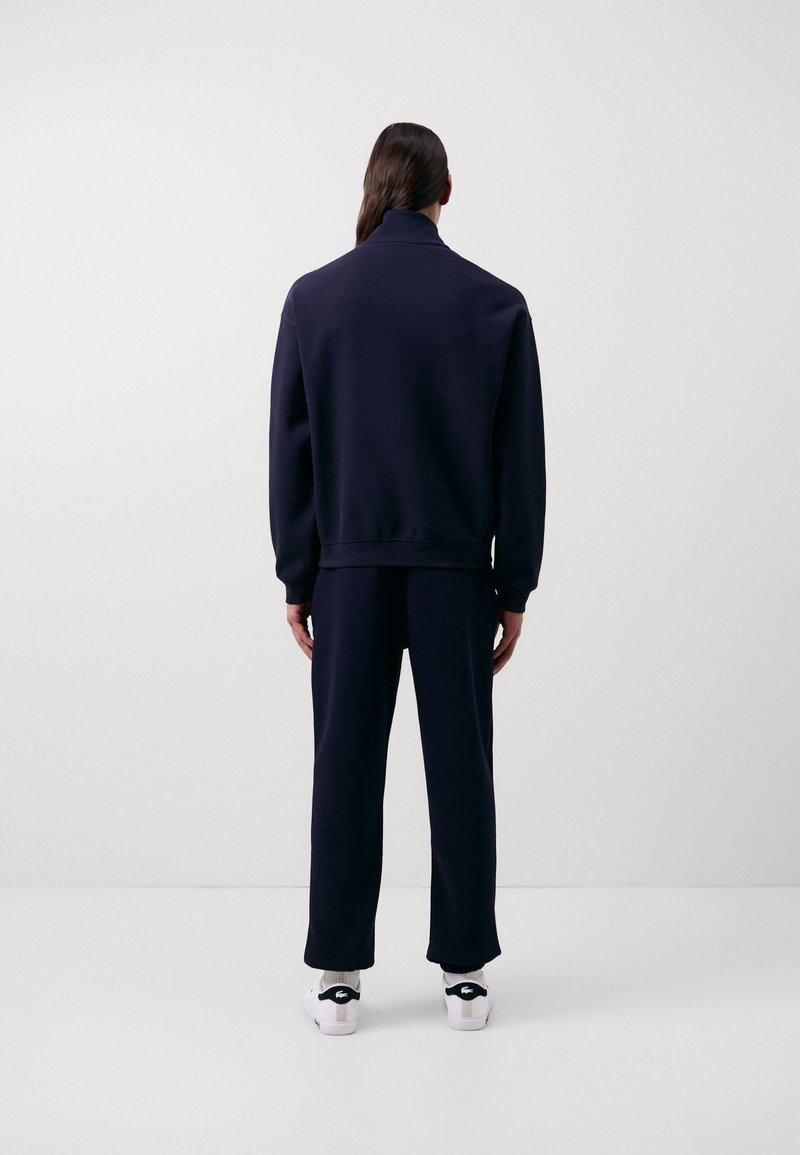 Sweatshirt bleu marine et pantalon assorti en tissu doux, présentant un col montant et des poignets côtelés, associés à des baskets blanches et noires.