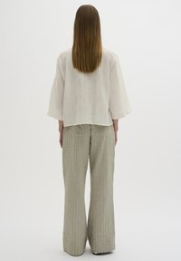 Blusa blanca texturizada con mangas anchas, combinada con pantalones sueltos de color verde claro con rayas verticales y patrones en relieve.