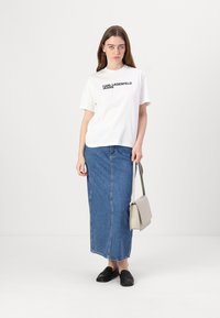 Biely bavlnený tričko s potlačou "KARL LAGERFELD JEANS" v čiernej farbe, skombinované s dlhou modrou džínovou sukňou. Čierne nazúvacie topánky a béžová kabelka.