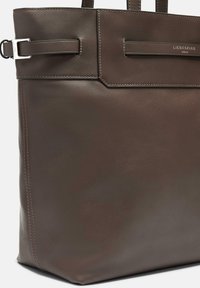 Brun läder tote-väska med plana handtag, som har en slick yta, fyrkantig form och en subtil, kontrasterande söm längs kanterna.