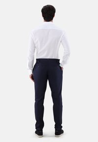 Camicia a quadri bianchi abbinata a pantaloni blu navy. I pantaloni sono dotati di due tasche posteriori e hanno una texture liscia, con passanti per cintura visibili.