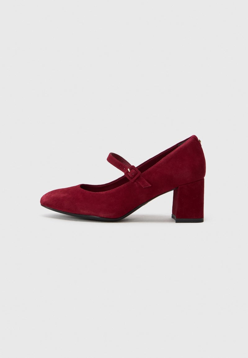 Chaussure Mary Jane en daim rouge avec bout arrondi, petit talon carré et bride réglable sur fond gris clair.