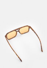 Lunettes de soleil écaille de tortue marron avec des verres rectangulaires, teinte ambre, et des branches élégantes avec des découpes. Matériau en plastique léger.