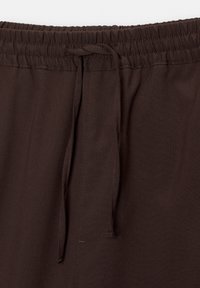 Pantalon marron foncé avec une taille élastique et un cordon de serrage noué au centre devant.