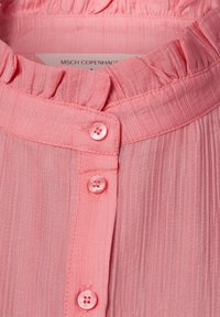 Lichtroze blouse met een gerimpelde halslijn, verticale gestructureerde stof en vijf bijpassende knopen langs de voorpanden.