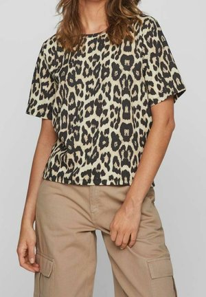 Woman wearing a short-sleeve leopard print top and beige cargo pants, standing with one hand near her pocket.