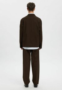 Brun oversized jakke med rett passform, kombinert med brune vide bukser. Hvit skjorte under med subtile striper.