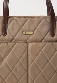 Beige gequilted handtas met diamantstiksel, bruine leren handvaten en een klein gouden Barbour-merkplaatje aan de voorkant.