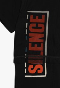 Czarny t-shirt z wyraźnym nadrukiem "SILENCE" w czerwonym i białym kolorze, otoczony niebieskimi i białymi akcentami, wykonany z miękkiego materiału.