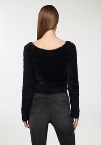 Maglione nero e morbido con design off-the-shoulder, maniche lunghe e fit corto, abbinato a jeans skinny grigio scuro.
