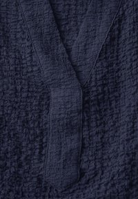 Tessuto blu marino con una texture rugosa e un aspetto sgualcito, caratterizzato da un design a V e pannelli frontali sovrapposti.
