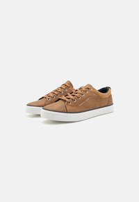 Brown lace-up sneakers with a smooth texture, featuring a white rubber sole and contrasting dark blue accents at the heel and toe.