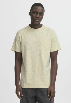 Short-sleeve beige t-shirt with a small chest pocket, featuring a speckled pattern in green, blue, and brown. Soft cotton fabric.