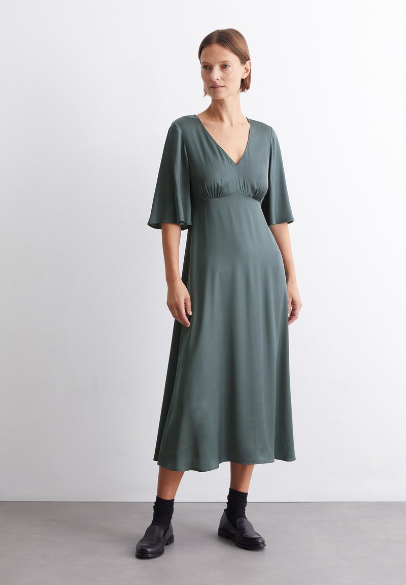 Langes, dunkelgrünes Kleid aus glattem, leichtem Stoff; verfügt über einen V-Ausschnitt, kurze, schwingende Ärmel und ein tailliertes Oberteil mit Raffung.