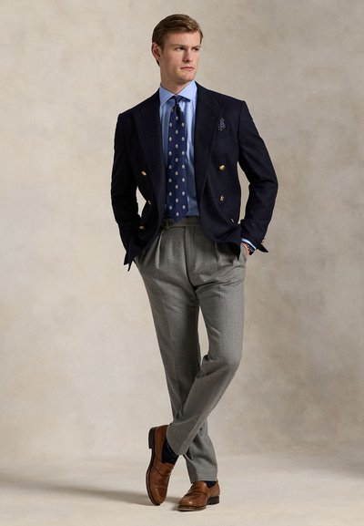 Sacou dublu cu nasturi aurii, cămașă bleu, cravată cu model, pantaloni gri, pantofi maro și șosete navy. Fundal texturat.