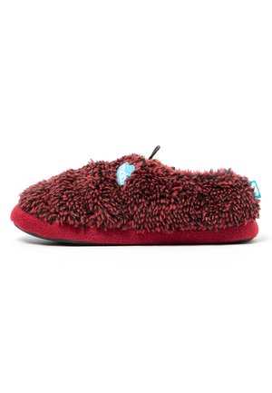 Zapatilla suave y peluda roja y negra con una suela gruesa y una pequeña etiqueta azul en el lateral, mostrada desde el perfil exterior.