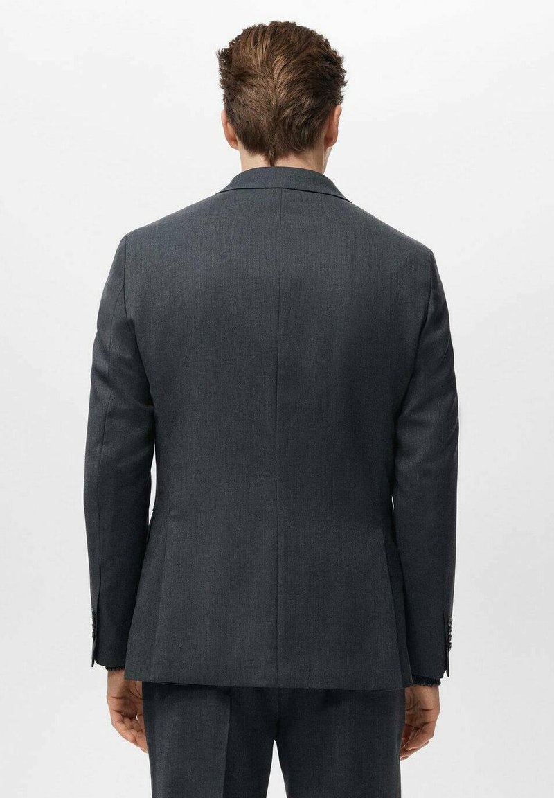 Giacca da uomo su misura in grigio scuro con spalle strutturate, tessuto liscio e spacco singolo sul retro. Dettaglio di cuciture discrete.