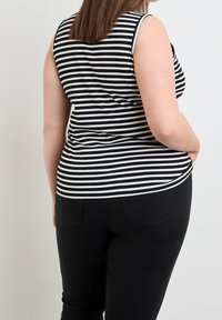 Černobílé pruhované tílko bez rukávů s přiléhavým střihem, žebrovanou strukturou a kulatým lemem, které je zkombinováno s černými džíny.