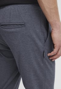 Pantalons de jogging gris texturé avec poches latérales et une petite étiquette de marque le long de la couture. Le tissu semble doux et extensible.