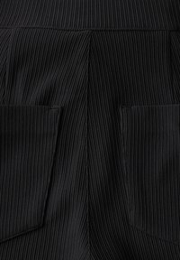 Tessuto nero strutturato con riga verticale, dotato di due tasche a toppa sui lati. Il design enfatizza un aspetto strutturato e sartoriale.