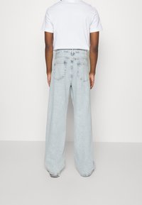 Světle modré široké džíny z denimu s vysokým pasem, pěti kapsami a viditelným šitím. Nošeny s jednoduchým bílým tričkem.
