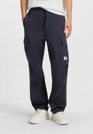 Navy cargo pants made of lightweight fabric, featuring elastic waistband, multiple pockets, and a relaxed fit, worn with white sneakers.