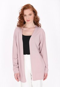Cardigan lungo a maniche lunghe di colore rosa chiaro con apertura davanti, texture morbida e vestibilità comoda, indossato sopra un top nero e pantaloni bianchi.
