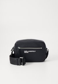 Borsa a tracolla nera realizzata in materiale sintetico testurizzato. Presenta una tasca frontale con zip, hardware argentato e una tracolla regolabile con logo.