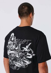 Camiseta de algodón negra con un estampado gráfico en la parte posterior que representa una figura, estrellas y pájaros en blanco, con un corte relajado y mangas cortas.