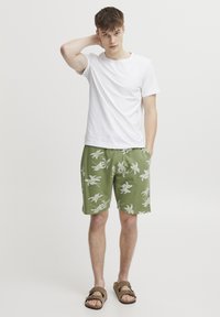 T-shirt bianca in cotone a maniche corte abbinata a pantaloni corti verde oliva con una stampa floreale bianca e sandali marroni.