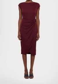Burgundy, knälång klänning med en figursydd silhuett, korta ärmar och en sidovridning som säkras av två metalliska detaljer. Slät tygstruktur.