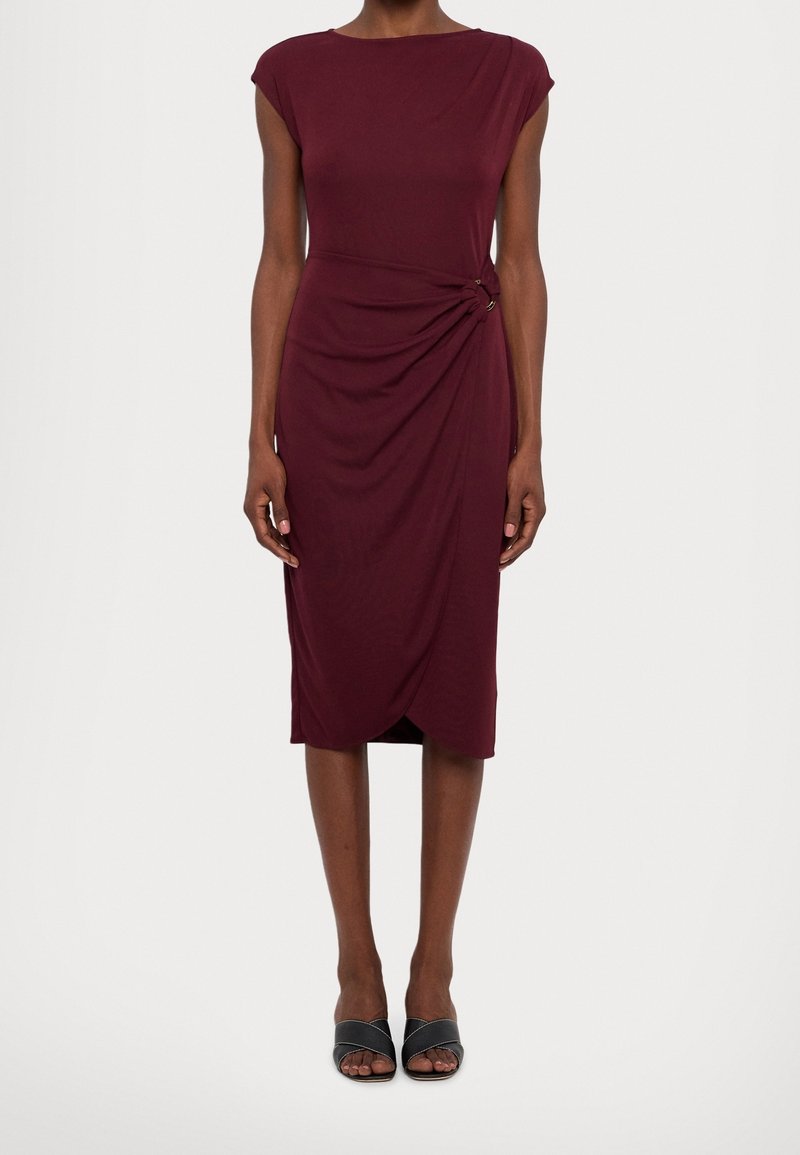 Burgundy, knälång klänning med en figursydd silhuett, korta ärmar och en sidovridning som säkras av två metalliska detaljer. Slät tygstruktur.