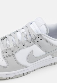 Baskets Nike blanches et gris clair avec lacets, logo Nike swoosh brodé et détails rembourrés sur la languette et le col.