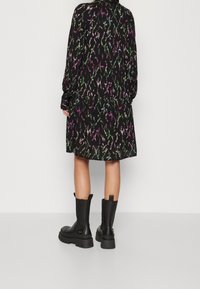 Czarna sukienka z kolorowym, bogatym wzorem; z długimi rękawami i luźnym krojem. Połączona z czarnymi botkami za kostkę na grubym spodzie.