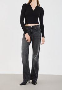 Haut noir côtelé à manches longues avec un col en V, associé à un jean gris à jambes larges. Tenue complétée par des escarpins noirs pointus.