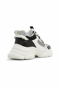 Sneaker chunky con tacco in pelle nera, tomaia in rete bianca, dettagli grigi, suola spessa bianca e una linguetta sul retro per una facile calzata.