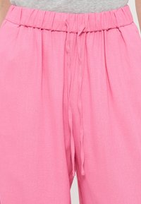 Ροζ φαρδιά παντελόνια με ελαστική μέση και κορδόνι, φορεμένα με ανοιχτό γκρι τοπ.