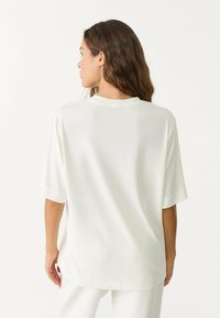 Volný, krátký rukávový top z hladkého off-white materiálu, s kulatým výstřihem a uvolněným siluetou, s jemným leskem.