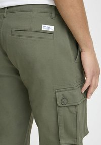 Groene katoenen cargobroek met een zijzak met twee knopen, een achterzak en een label met de tekst "BLEND." Glad textuur, casual ontwerp.