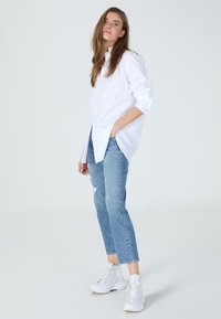 Weiß gestreifte Button-Up-Bluse kombiniert mit hellblauen, getragenen Jeans und weißen High-Top-Sneakern. Lässiger und lockerer Schnitt.