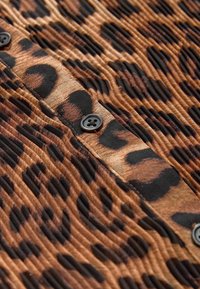 Tela con estampado de leopardo y textura estriada, con una combinación de colores marrón y negro. Cerca del borde se observa un botón negro.