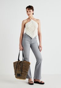 White crochet halter top with a diamond pattern, paired with light gray flared jeans. Accessories include a striped black and yellow tote bag.