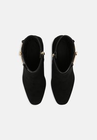 Bottines en daim noir avec un toe pointu, fermeture éclair latérale et accents en métal doré. Texture lisse et design épuré.