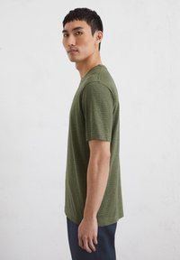Green striped t-shirt with short sleeves and a crew neckline, made of lightweight fabric, featuring a ribbed texture and a relaxed fit.