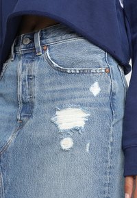 Ljust blå denimkjol med slitna områden, fransade kanter och hög midja. I kombination med en marinblå långärmad topp.